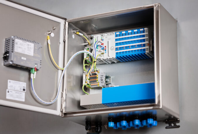 Geöffnete Schalttafel aus Edelstahl mit komplexen Elektro Arbeiten, Verkabelungssystemen und Schaltschränken, geeignet für Mittel- und Hochspannungsanlagen im Industrie Bereich. Die Installation zeigt sorgfältig verlegte Leitungen und modulare Komponenten, die auch Glasfaserarbeiten und Anwendungen in Erneuerbaren Energien unterstützen.