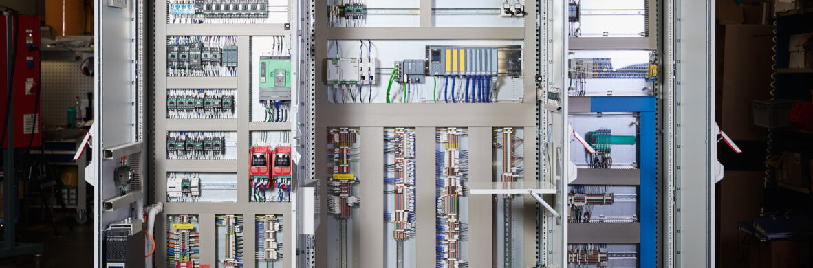 Offene Schaltschränke in einer Industrieanlage zeigen komplexe Elektro Arbeiten mit Verkabelungssystemen und Schalttafeln. Die Installation umfasst Mittel- und Hochspannungsanlagen sowie Glasfaserarbeiten, die für den Bereich Erneuerbare Energien optimiert sind.