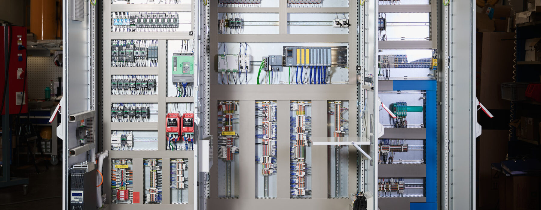 Offene Schaltschränke in einer Industrieanlage zeigen komplexe Elektro Arbeiten mit Verkabelungssystemen und Schalttafeln. Die Installation umfasst Mittel- und Hochspannungsanlagen sowie Glasfaserarbeiten, die für den Bereich Erneuerbare Energien optimiert sind.