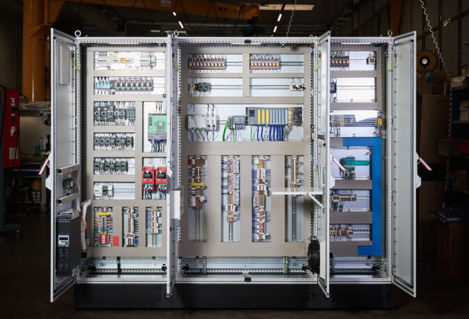 Offene Schaltschränke in einer Industrieanlage zeigen komplexe Elektro Arbeiten mit Verkabelungssystemen und Schalttafeln. Die Installation umfasst Mittel- und Hochspannungsanlagen sowie Glasfaserarbeiten, die für den Bereich Erneuerbare Energien optimiert sind.