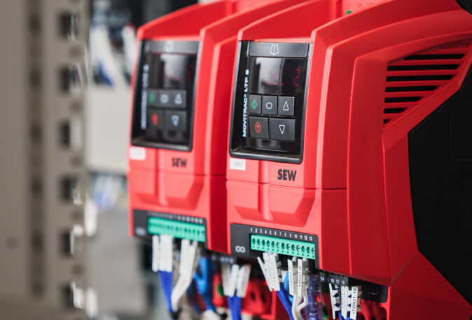 Nahaufnahme von roten Frequenzumrichtern in einem Schaltschrank mit angeschlossenen Verkabelungssystemen, typisch für Elektro Arbeiten im Industrie Bereich, Mittel- und Hochspannungsanlagen sowie Glasfaserarbeiten und Erneuerbare Energien.