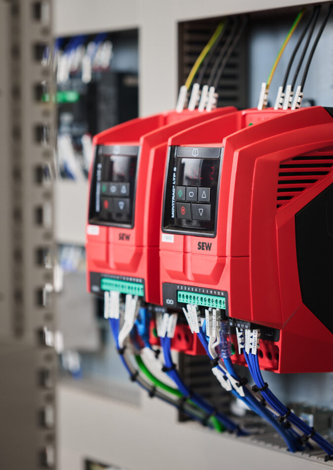 Nahaufnahme von roten Frequenzumrichtern in einem Schaltschrank mit angeschlossenen Verkabelungssystemen, typisch für Elektro Arbeiten im Industrie Bereich, Mittel- und Hochspannungsanlagen sowie Glasfaserarbeiten und Erneuerbare Energien.