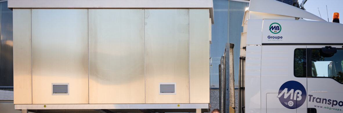 Auf einem Lastwagen wird eine vormontierte Überwachungskabine aus Metall transportiert, die als witterungsbeständige Sicherheitskabine mit thermischer Isolierung dient. Die anschlussfertige Kabine ist ein Beispiel für den Kabinenbau für Bahntechnik und gehört zur Infrabel Loge PNBA. Sie wurde im Rahmen von Prototypenbau und Serienfertigung hergestellt.