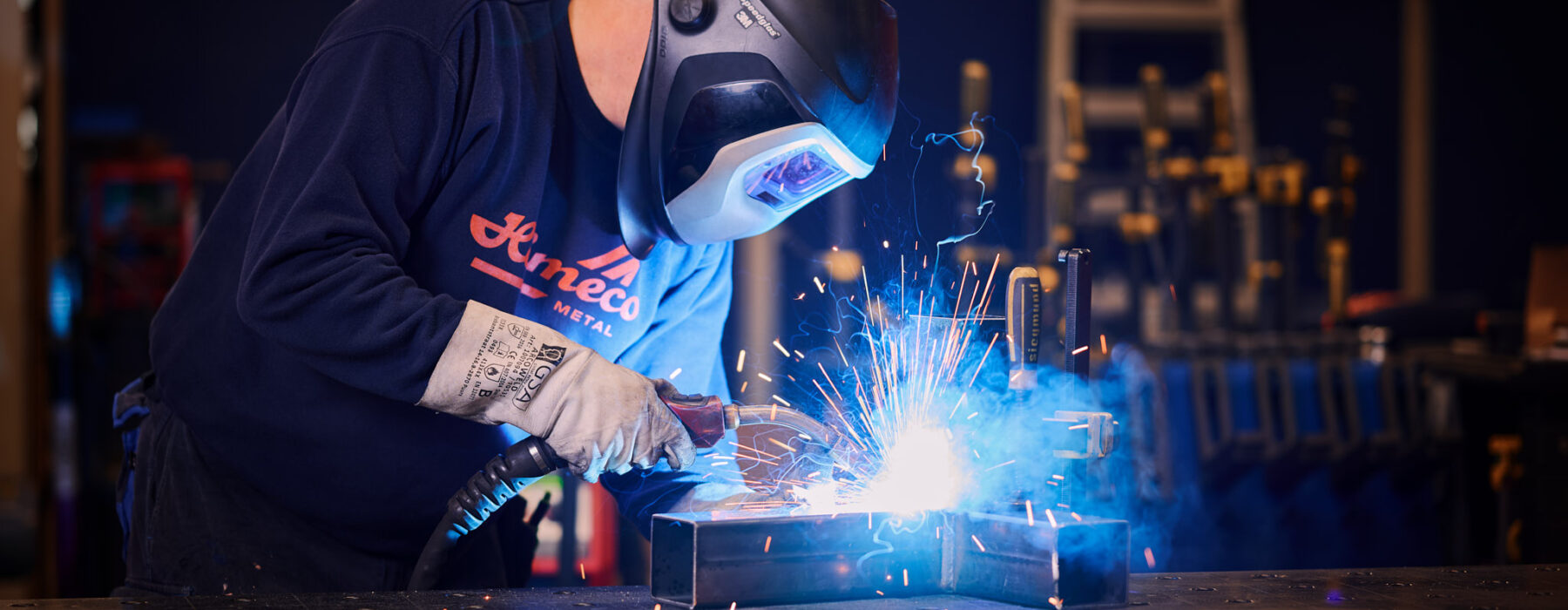 Metallbauer bei präziser Schweißarbeit an Metallrahmen mit Schutzhelm und Handschuhen
