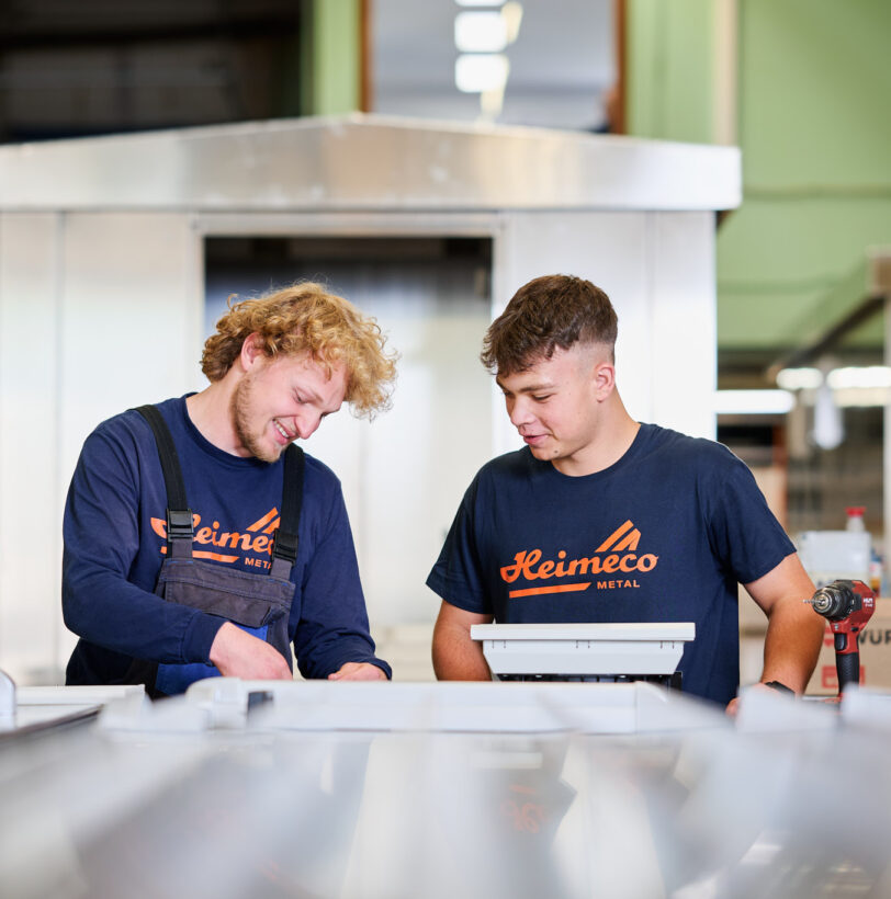 Zwei junge Fachkräfte im Metallbau arbeiten gemeinsam an einem Blechprojekt in einer Werkstatt. Sie führen Maßarbeit mit hoher Präzision aus und nutzen ihre Erfahrung in der Planung, Konstruktion und Fertigung. Die Blechverarbeitung erfolgt mit modernen Werkzeugen, was für Qualität und professionelle Produktion steht.