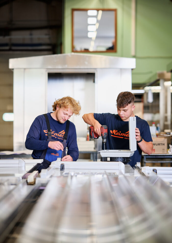 Zwei Facharbeiter im Metallbau führen Maßarbeit an Blechkomponenten durch. Sie arbeiten konzentriert mit Werkzeugen an der Fertigung und Montage in einer modernen Werkstatt. Die Planung, Konstruktion und Produktion der Bauteile erfolgt mit hoher Qualität und langjähriger Erfahrung in der Blechverarbeitung.
