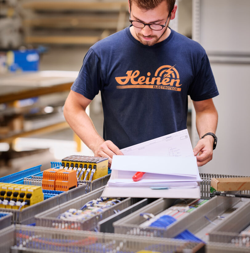 Ein Techniker prüft Elektro Arbeiten an einer Schalttafel mit Schaltschränken und Verkabelungssystemen in einer Industrie Umgebung, die auch Mittel- und Hochspannungsanlagen sowie Glasfaserarbeiten für Erneuerbare Energien umfasst.