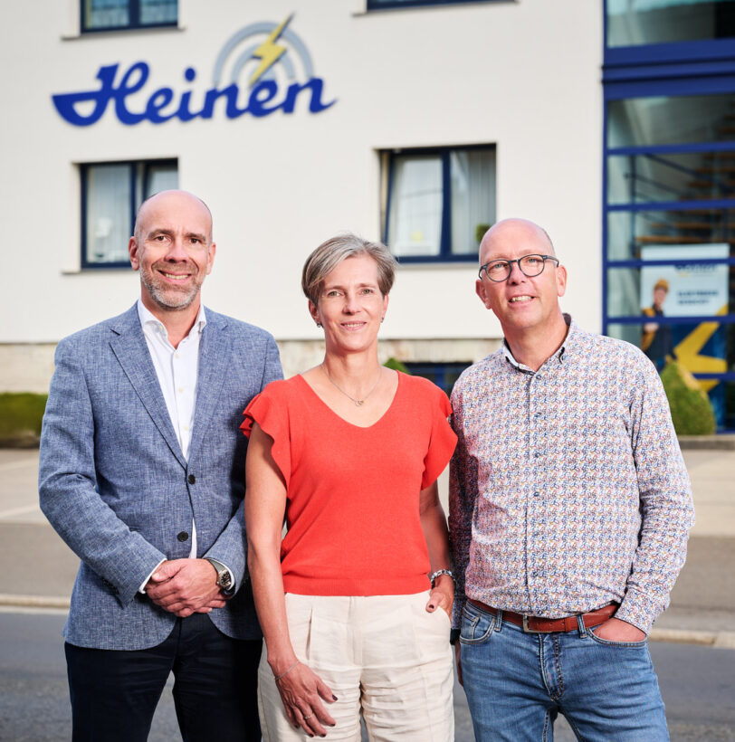 Drei Mitarbeitende der Heinen Group stehen vor dem Firmengebäude mit dem Schriftzug Heinen. Das private Familienunternehmen bietet ganzheitliche technische Lösungen in Elektrotechnik, Metallbau, Eisenbahntechnik und Industrietechnik aus einer Hand. Mit 70 Jahren Erfahrung ist Heinen Electrotech, Heimeco Metal und Cable Works ein innovatives Unternehmen und zertifizierter Partner in den Bereichen Elektrotechnik Metallbau Eisenbahn.