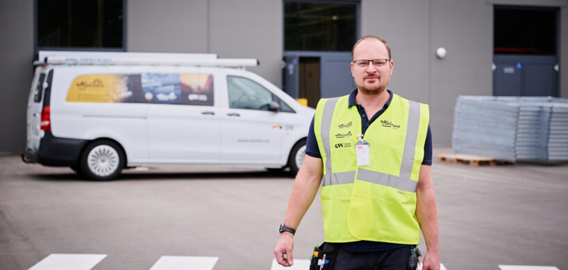 Ein zentraler Ansprechpartner in Warnweste steht vor einem Firmenfahrzeug und hält einen Werkzeugkoffer. Die vereinte Kompetenz des Mitarbeiters zeigt sich durch vielseitige und durchdachte Beratung. Transparent und lösungsorientiert unterstützt er Kunden vor Ort.