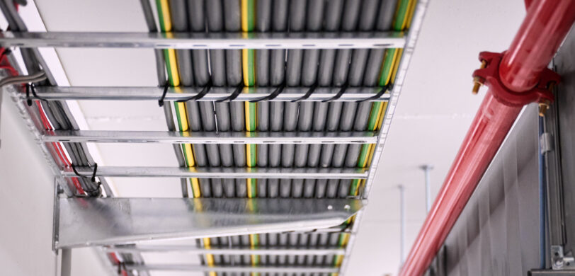 Detailaufnahme der Elektroinstallation in den NMC Neue Hallen Eynatten mit Kabeltrassen für Schaltschränke und Unterverteilungen im Industrieneubau. Zu sehen sind sorgfältig verlegte Leitungen für Niederspannungsverteilung, Daten- und IT-Verkabelung Produktion sowie Installationen für Brandmeldeanlagen und Industriebeleuchtung LED. Die Installation ist Teil eines Elektroinstallation Großprojekts inklusive Schaltanlagenbau und Anschluss Produktionslinien.