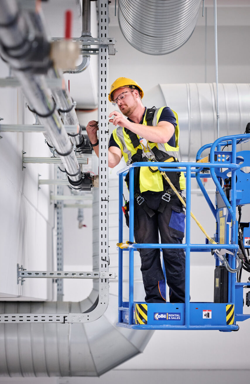 Elektriker auf Hebebühne installiert Elektrotechnik in Industriehalle NMC Neue Hallen Eynatten