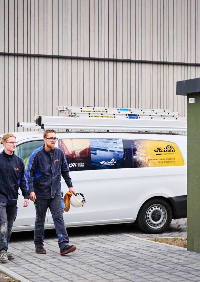 Elektriker vor Sporthalle Schönefeld Eupen mit Firmenfahrzeug und moderner Elektrotechnik