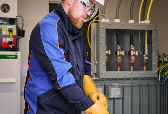 Elektriker zieht Isolierhandschuhe an vor Schaltschrank in Sporthalle Schönefeld Eupen