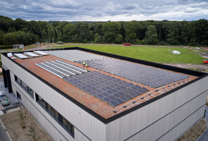 Die Sporthalle Schönefeld Eupen zeigt ihre moderne Elektrotechnische Ausstattung mit einer großen Photovoltaikanlage auf dem Dach. Die barrierefreie Mehrzweckhalle ist umgeben von Grünflächen und verfügt über intelligente LED-Beleuchtung, IT-Verkabelung und umfassende Sicherheitstechnik, die den nachhaltigen und sicheren Betrieb gewährleisten.
