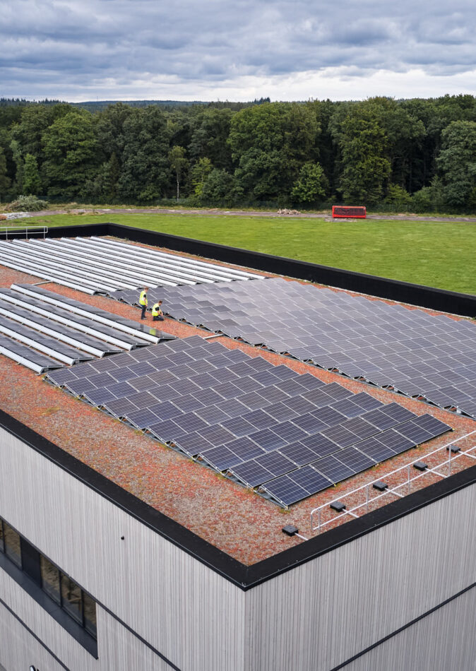 Die Sporthalle Schönefeld Eupen zeigt ihre moderne Elektrotechnische Ausstattung mit einer großen Photovoltaikanlage auf dem Dach. Die barrierefreie Mehrzweckhalle ist umgeben von Grünflächen und verfügt über intelligente LED-Beleuchtung, IT-Verkabelung und umfassende Sicherheitstechnik, die den nachhaltigen und sicheren Betrieb gewährleisten.