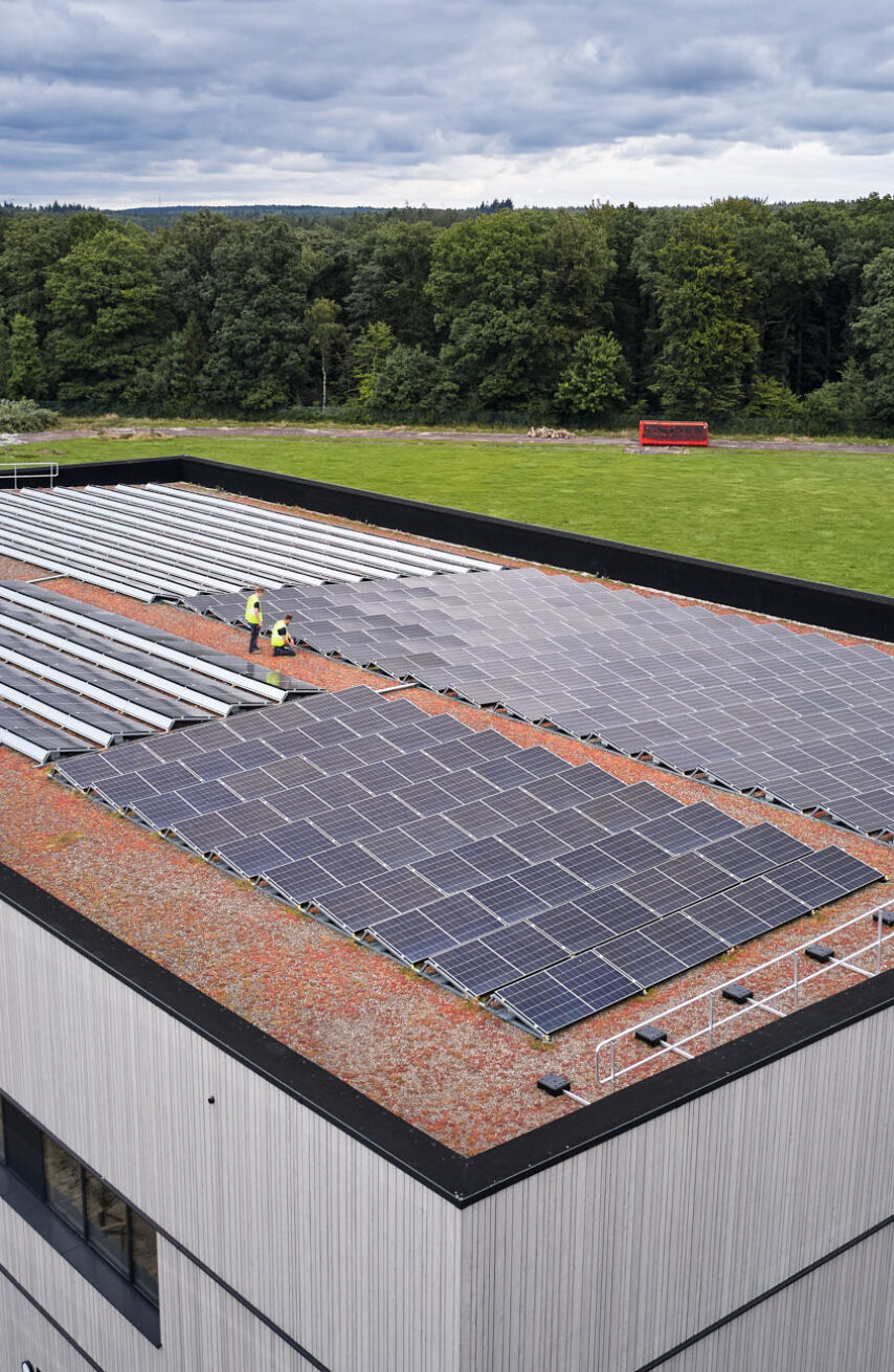 Die Sporthalle Schönefeld Eupen zeigt ihre moderne Elektrotechnische Ausstattung mit einer großen Photovoltaikanlage auf dem Dach. Die barrierefreie Mehrzweckhalle ist umgeben von Grünflächen und verfügt über intelligente LED-Beleuchtung, IT-Verkabelung und umfassende Sicherheitstechnik, die den nachhaltigen und sicheren Betrieb gewährleisten.