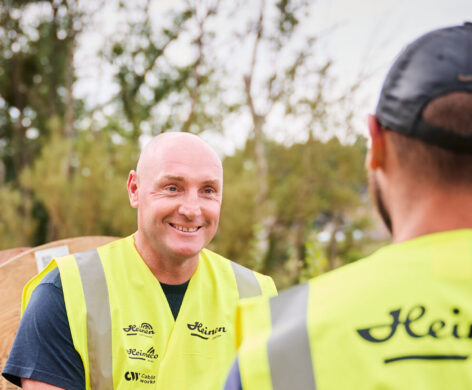 Zwei Handwerker in leuchtend gelben Warnwesten mit dem Logo Heinen sitzen und unterhalten sich vor einem Transporter und großen Kabeltrommeln. Als zentraler Ansprechpartner zeigen sie vereinte Kompetenz und bieten durchdachte, transparente Beratung. Die Szene vermittelt eine vielseitige und lösungsorientierte Zusammenarbeit im Außeneinsatz.