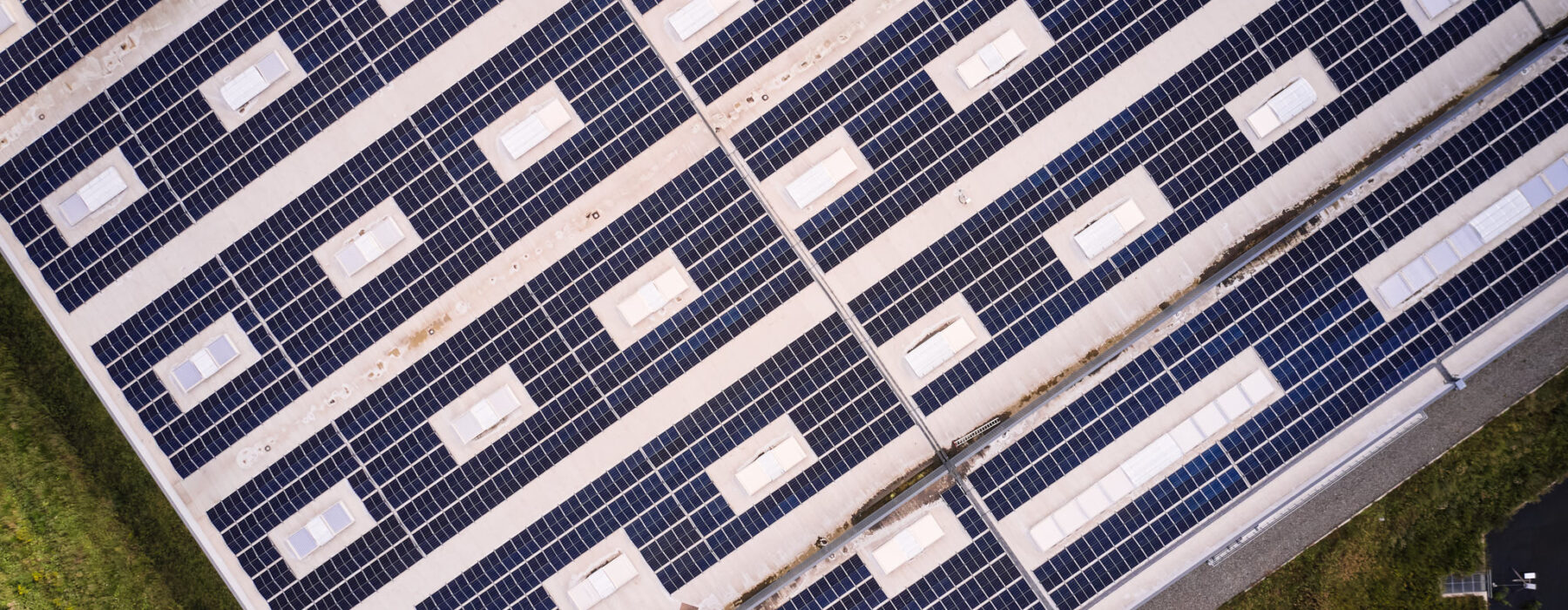 Drohnenaufnahme einer industriellen Photovoltaikanlage auf dem Dach einer großen Industriehalle, Teil der Elektrotechnik im Sägewerk IBV Vielsalm. Die Anlage ist Teil der elektrotechnischen Ausstattung für Holzindustrie und dient der Einspeisung in das öffentliche Mittelspannungsnetz. Die Integration der Photovoltaikanlage erfolgt gemäß Lastenheft und unterstützt die industrielle Energieverteilung. Glasfaser Leitungen für Industrie und Kopfstationen sind ebenfalls Bestandteil der Infrastruktur. Das Blockheizkraftwerk für Industrie ist in das bestehende Mittelspannungsnetz integriert, um eine effiziente Energieversorgung sicherzustellen.