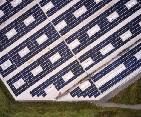 Drohnenaufnahme einer industriellen Photovoltaikanlage auf dem Dach einer großen Industriehalle, Teil der Elektrotechnik im Sägewerk IBV Vielsalm. Die Anlage ist Teil der elektrotechnischen Ausstattung für Holzindustrie und dient der Einspeisung in das öffentliche Mittelspannungsnetz. Die Integration der Photovoltaikanlage erfolgt gemäß Lastenheft und unterstützt die industrielle Energieverteilung. Glasfaser Leitungen für Industrie und Kopfstationen sind ebenfalls Bestandteil der Infrastruktur. Das Blockheizkraftwerk für Industrie ist in das bestehende Mittelspannungsnetz integriert, um eine effiziente Energieversorgung sicherzustellen.