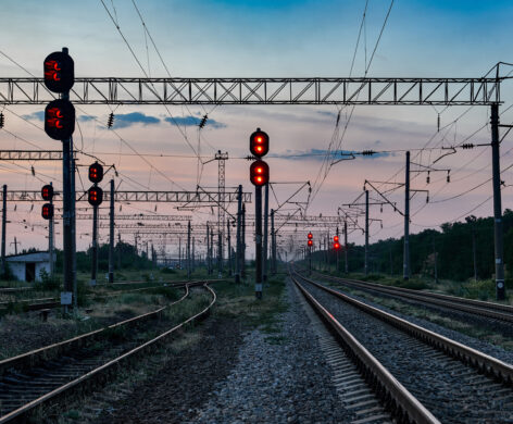 Blick auf ein komplexes Eisenbahnsignal- und Oberleitungssystem bei Dämmerung, das die Planung und Entwicklung sowie die elektrotechnische Beratung und Umsetzung in der Infrastruktur unterstützt. Die zahlreichen Signale und Leitungen zeigen die Bedeutung für Industrie und öffentliche Gebäude entlang der Bahnstrecke.