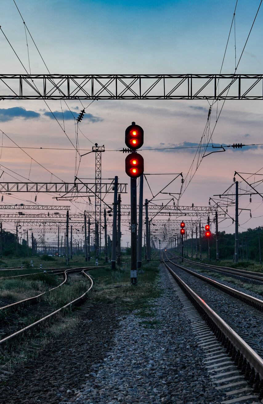 Blick auf ein komplexes Eisenbahnsignal- und Oberleitungssystem bei Dämmerung, das die Planung und Entwicklung sowie die elektrotechnische Beratung und Umsetzung in der Infrastruktur unterstützt. Die zahlreichen Signale und Leitungen zeigen die Bedeutung für Industrie und öffentliche Gebäude entlang der Bahnstrecke.
