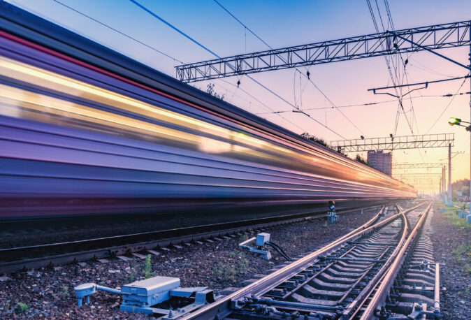 Schnellfahrender Zug auf Eisenbahngleis mit Kabelverlegung und Signaltechnik bei Sonnenuntergang
