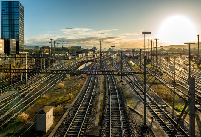 Weitläufiges Eisenbahngelände mit Gleisen, Oberleitungen und Signaltechnik bei Sonnenuntergang