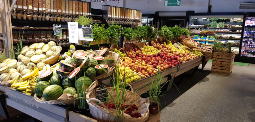 Ein moderner Einzelhandel mit frischem Obst wie Wassermelonen, Bananen, Äpfeln und Melonen, präsentiert in einem Geschäft mit gut organisierter Infrastruktur. Im Hintergrund sind Produktionsanlagen für lose Ware zu sehen, die durch Elektrotechnik gesteuert werden. Dieses Geschäft ist ein Beispiel für öffentliche Bauprojekte und öffentliche Gebäude, die verschiedene Sektoren der Industrie und des Großhandels bedienen.