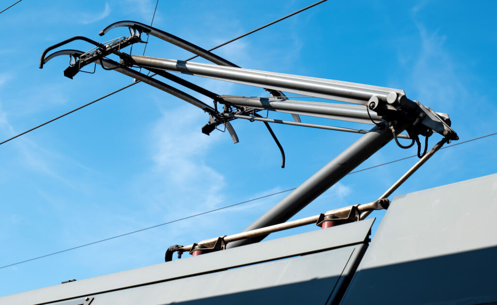 Nahaufnahme eines Stromabnehmers an einer Straßenbahn vor blauem Himmel, symbolisch für Planung und Entwicklung sowie elektrotechnische Beratung und Umsetzung in der Industrie, öffentlichen Gebäuden und Infrastruktur.