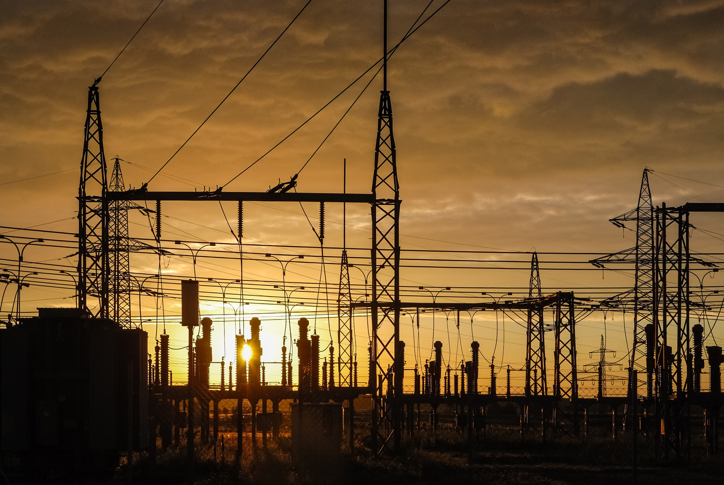 Ein Umspannwerk mit Mittel- und Hochspannungsanlagen bei Sonnenuntergang, das komplexe Verkabelungssysteme und Strommasten zeigt. Die Elektro Arbeiten umfassen Schalttafeln und Schaltschränke im Industrie Bereich, die essenziell für die Energieverteilung sind. Glasfaserarbeiten und moderne Technologien unterstützen die Integration von Erneuerbaren Energien in das Netz.