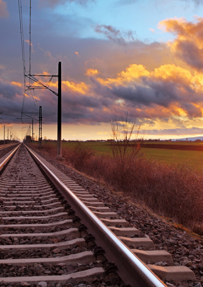 Eisenbahnstrecke bei Sonnenuntergang mit Oberleitungen für Elektrotechnische Arbeiten und Kabelverlegung